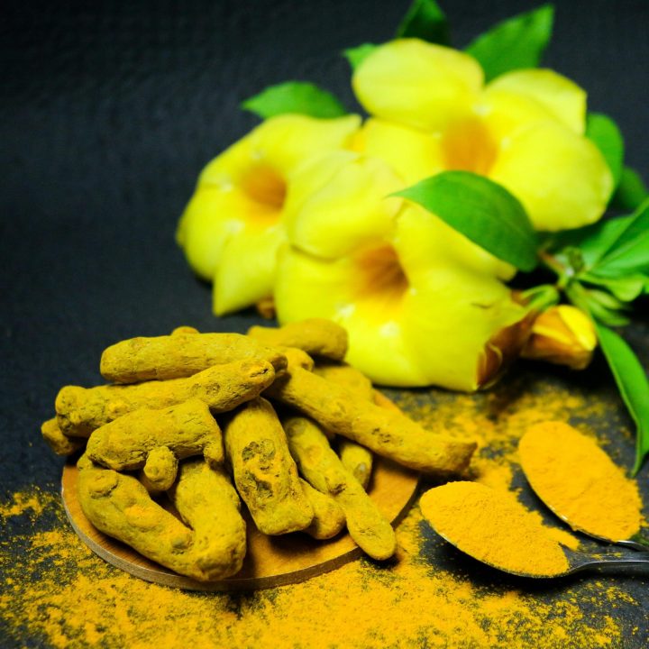 pexels-photo-7988014-7988014 Vivid close-up of turmeric roots and powder with yellow flowers on dark background.