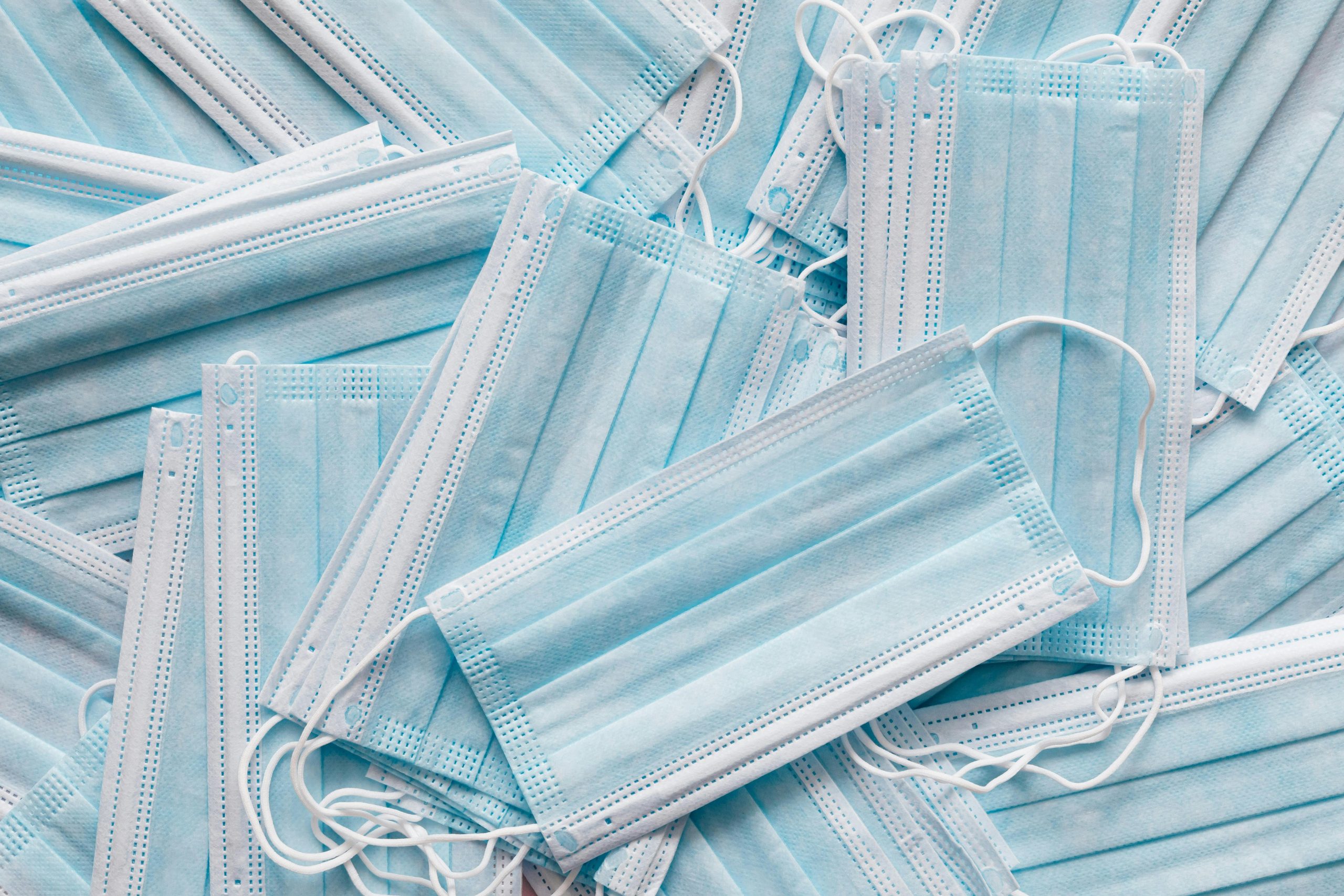 pexels-photo-4197564-4197564 Top view of many clean single use light blue surgical protective face mask lying on top of each other in disorder