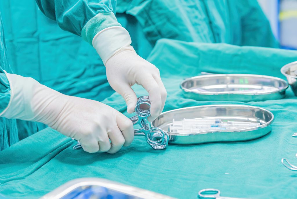 Close-up of a surgeon's gloved hands arranging instruments on a tray in an operating room.