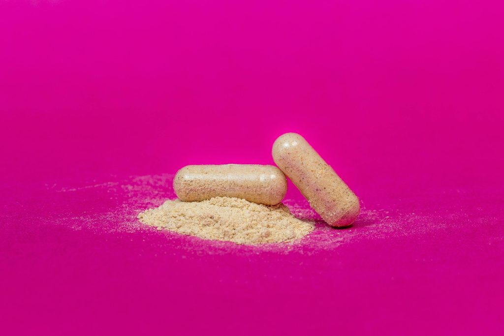 Close-up of two supplement capsules and powder on a vibrant pink background.