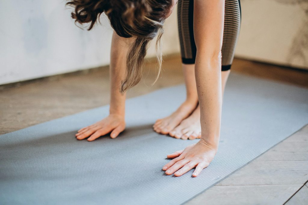 An adult woman performing a forward bend yoga pose indoors on a mat, focusing on flexibility and concentration.
