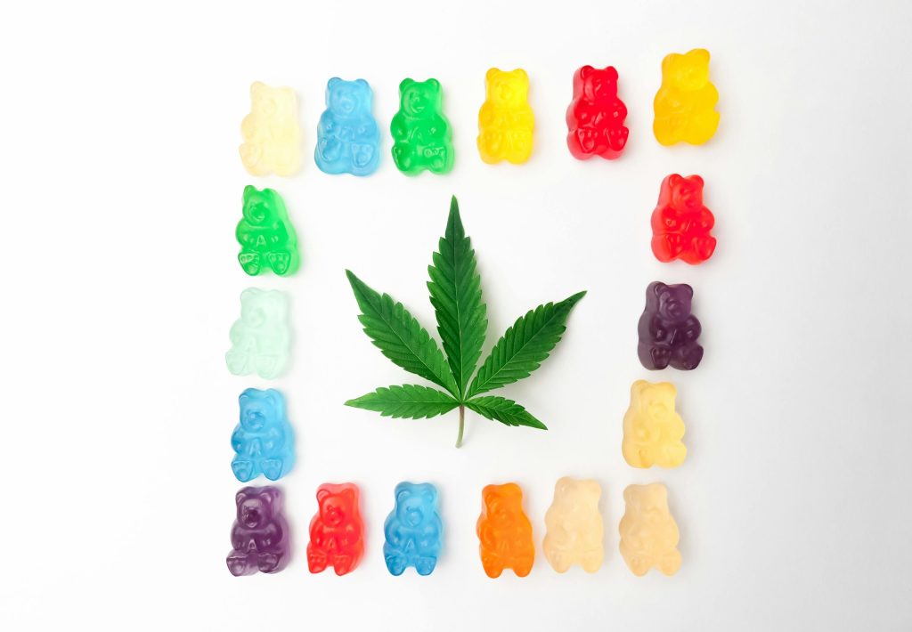 Vibrant gummy bears form a colorful border around a cannabis leaf on a white background, showcasing edible cannabis culture.