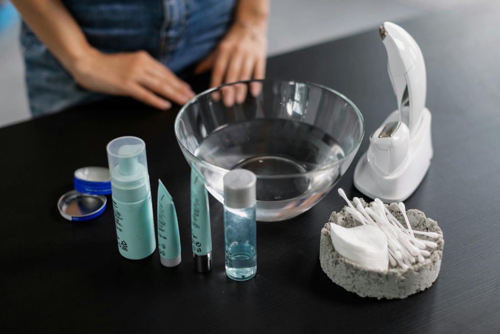 Flat lay of skincare products, tools, and a glass bowl on a black surface for beauty care routines.
